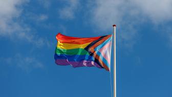 Proggresiivinen pride-lippu liehuu tuulessa sinisellä taivaalla