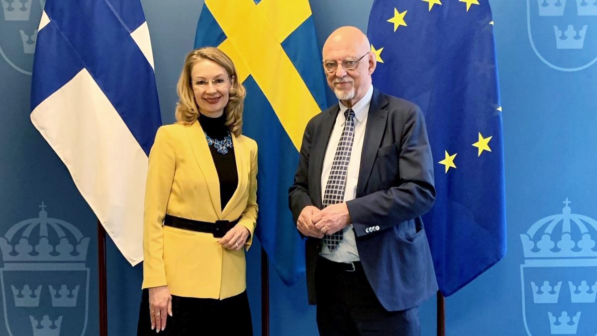 Ministers for European Affairs Hans Dahlgren and Tytti Tuppurainen standing on the front of Finnish, Swedish and EU flags