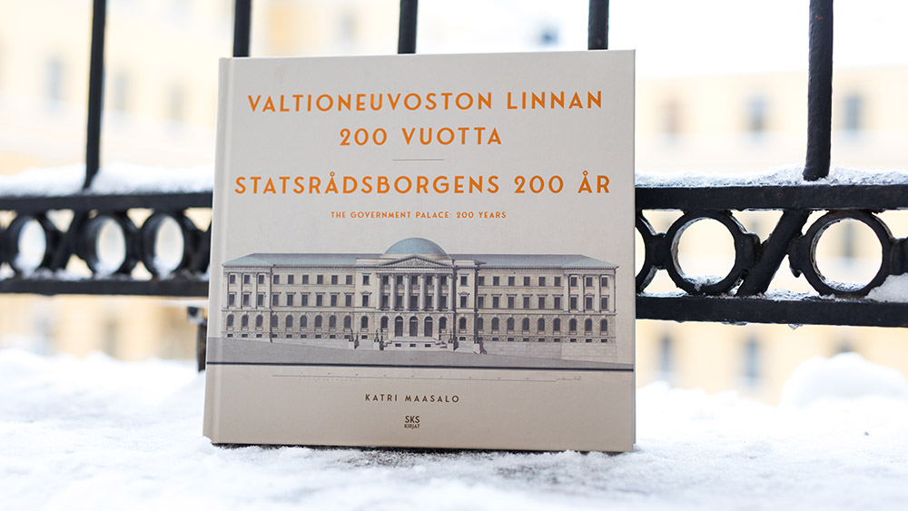 Kuvassa on kirja Valtioneuvoston linnan 200 vuotta Valtioneuvoston linnan talvisella sisäpihalla.