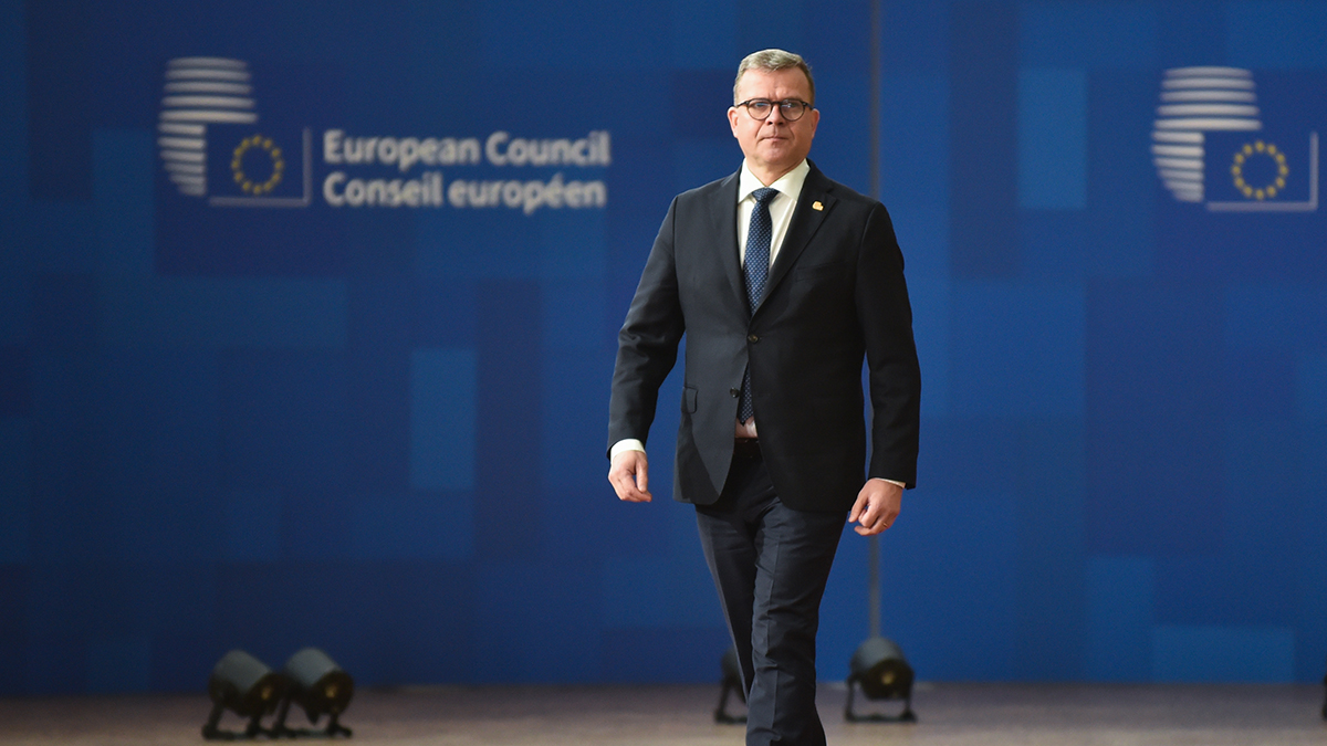 Kuvassa pääministeri Petteri Orpo kävelee taustanaan Eurooppa-neuvoston tunnus.