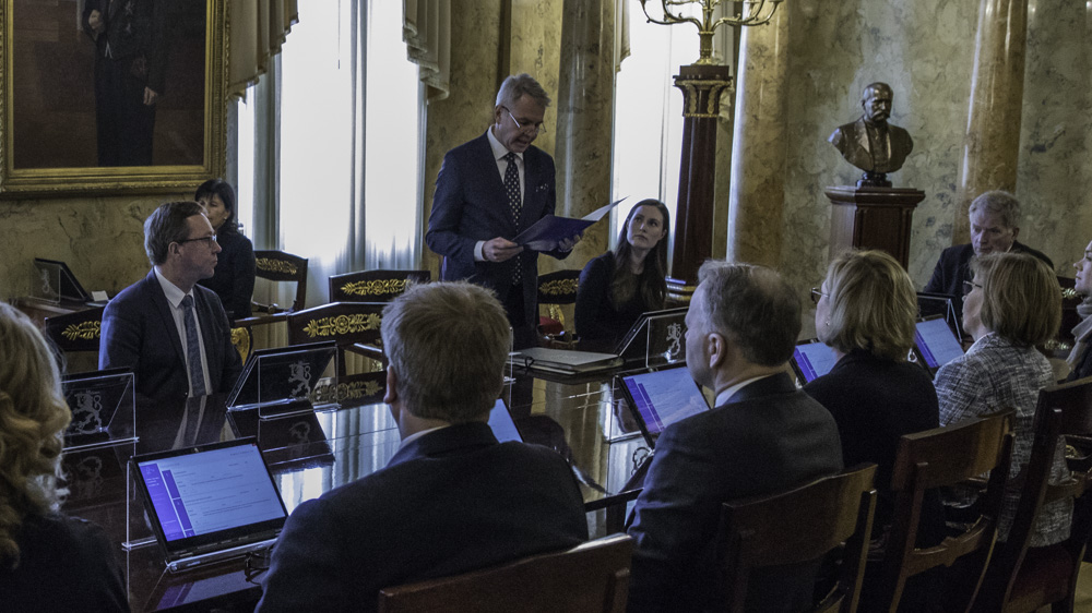 Ulkoministeri Pekka Haavisto lukee puhetta hallituksen ja presidentin kuunnellessa.
