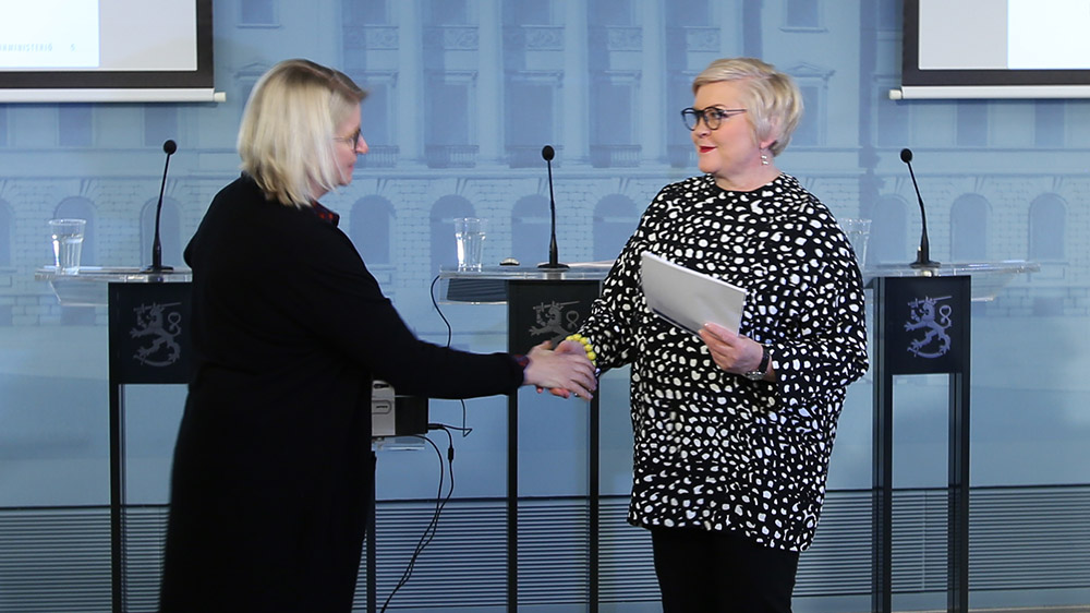 Auli Valli-Lintu luovuttaa selvityksen kunta- ja uudistusministeri Anu Vehviläiselle.