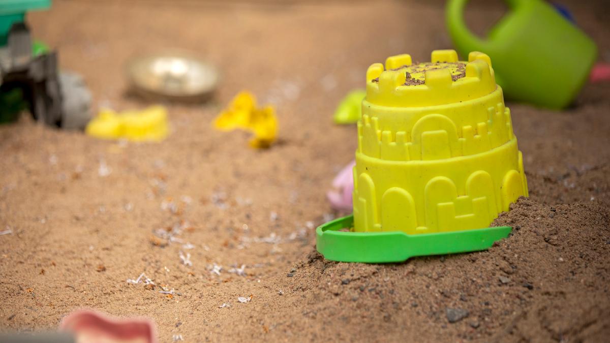 Keltainen ämpäri kumollaan hiekkalaatikolla, taustalla muita hiekkaleluja.