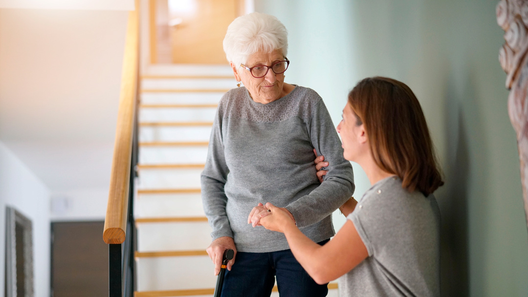 Hoitaja avustaa vanhusta portaissa.
