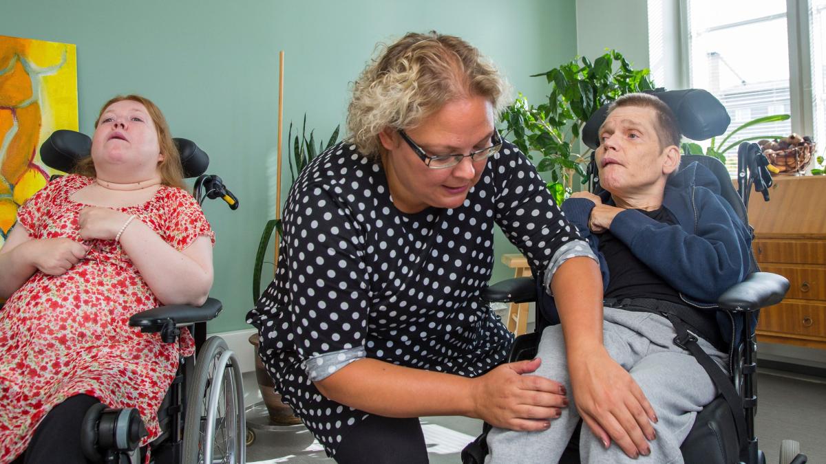Hoitaja auttaa miestä pyörätuolissa.