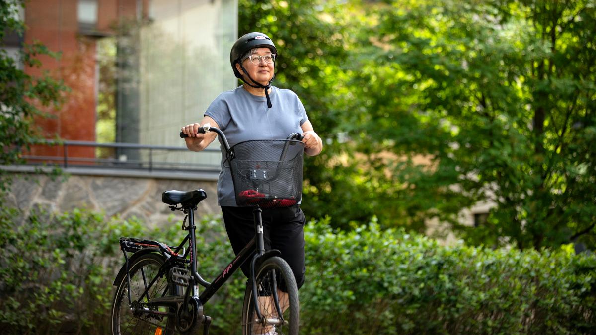 Kuvassa pyöräilijä taluttaa pyöräänsä kesäisessä maisemassa.