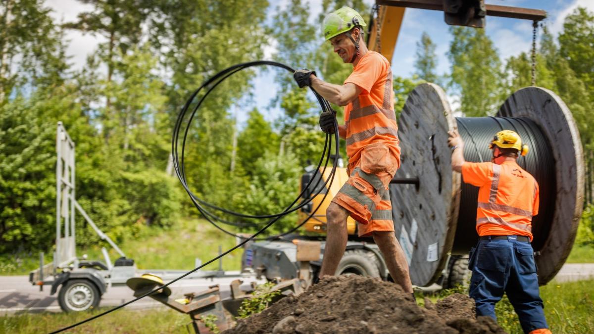 Kaksi miestä asentaa valokuitua tien varressa kesällä.