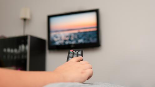 Kaukosäädin ihmisen kädessä ja televisio taustalla.