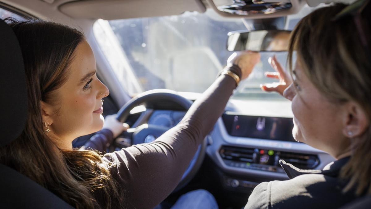 Nuori kuljettaja säätää auton taustapeiliä ajo-opettajan opastuksessa.