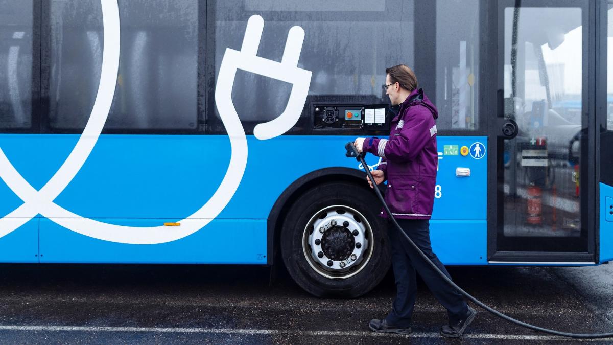 Mies lataa sähköbussia varikolla.