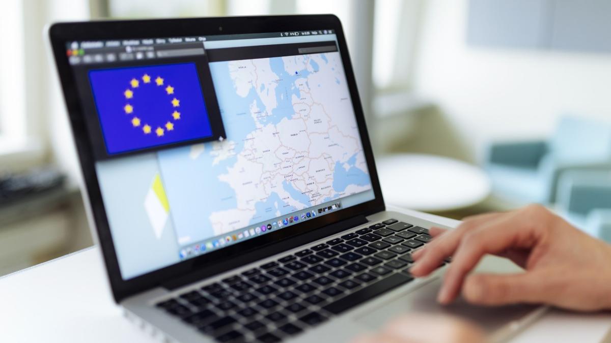 EU:n lippu ja kartta läppärin näytöllä, ihminen käsi näppäimistöllä.