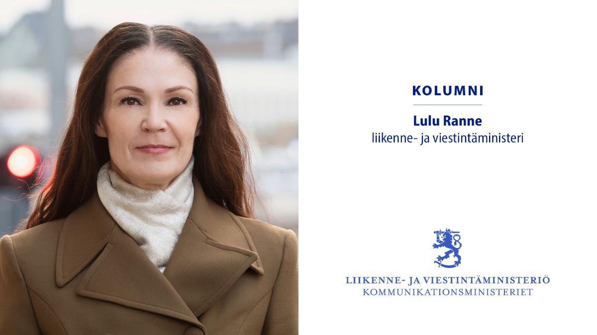 Ministeri Lulu Ranne takki ja kaulahuivi päällä aurinkoisena talvisena päivällä, taustalla kaupunkimaisemaa.