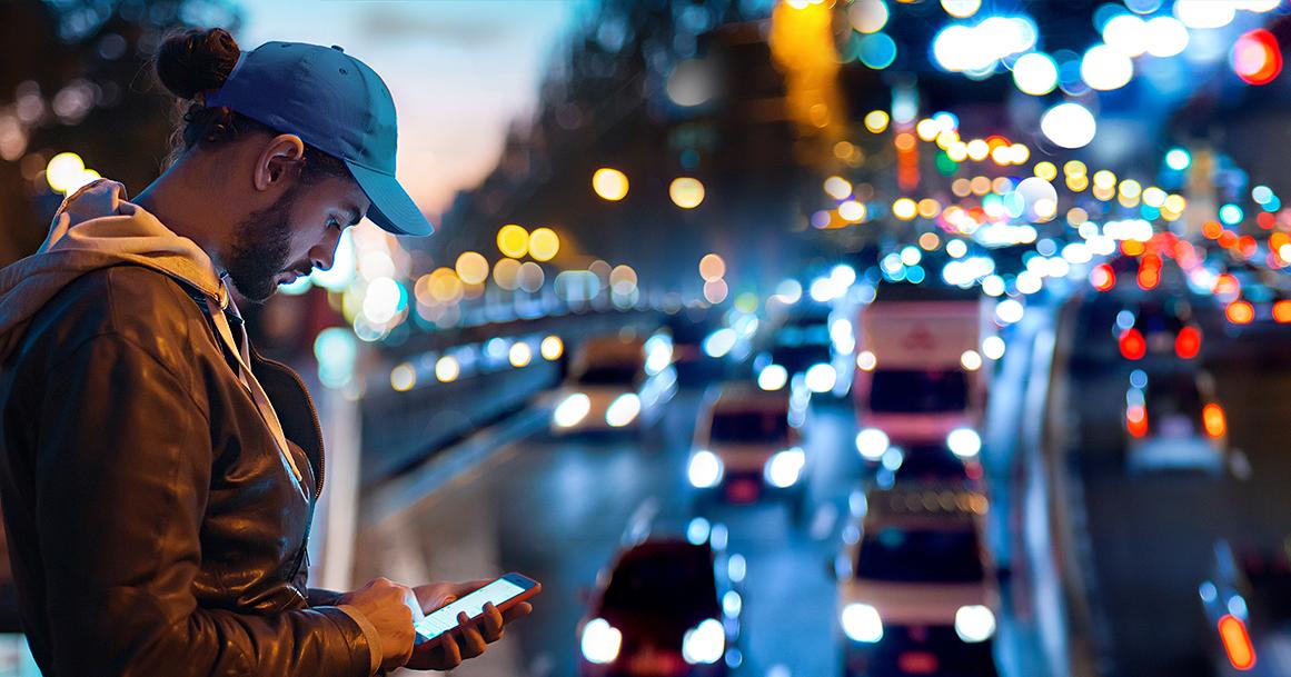 MIes tilaa puhelimella kyytiä, liikennettä taustalla. (Kuva:LVM)