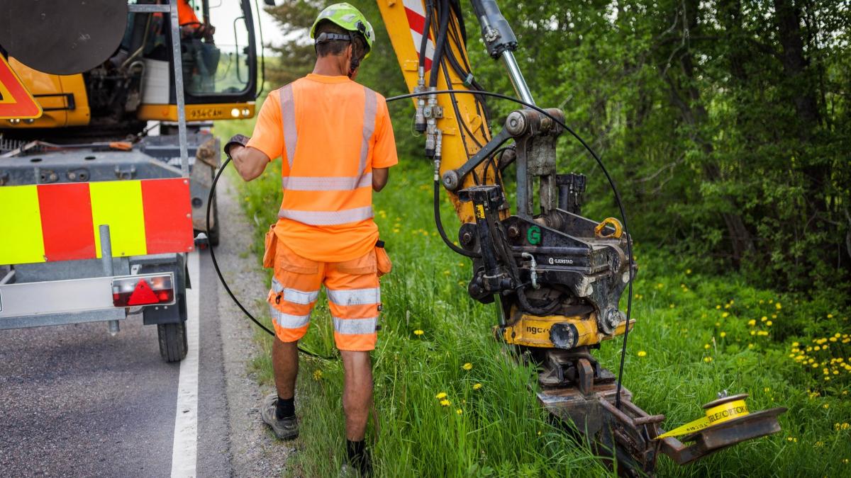 Kone ja työntekijä asentavat valokuitukaapelia maantien varteen.