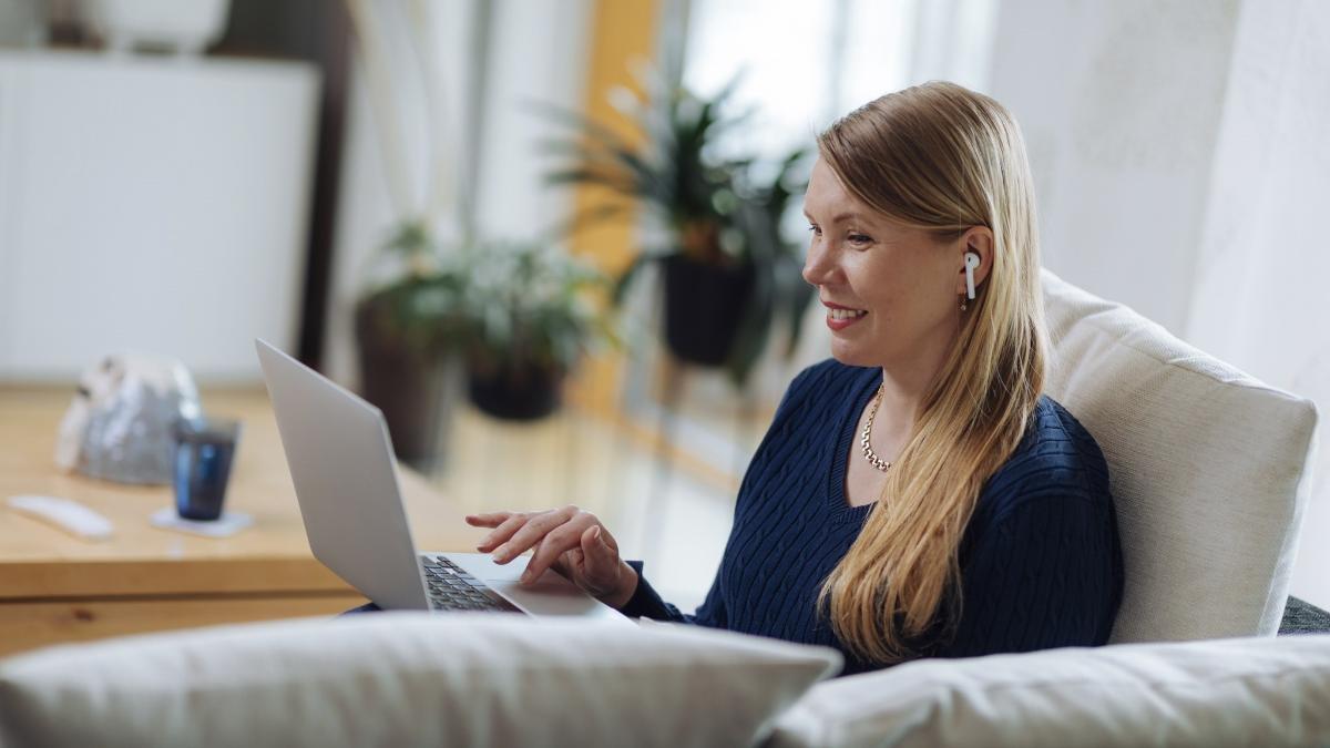 Iloinen nainen sohvalla kannettavan tietokoneen kanssa.