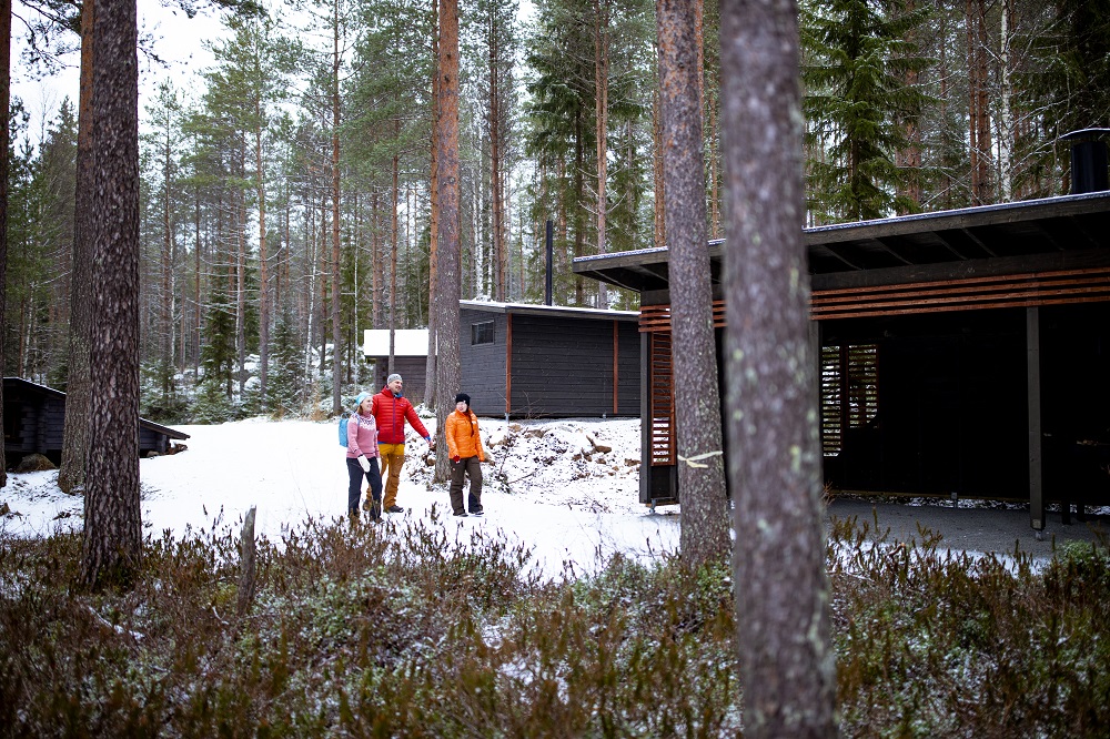 Kolme ihmistä kävelemässä talvisessa Evossa rakennusten välillä