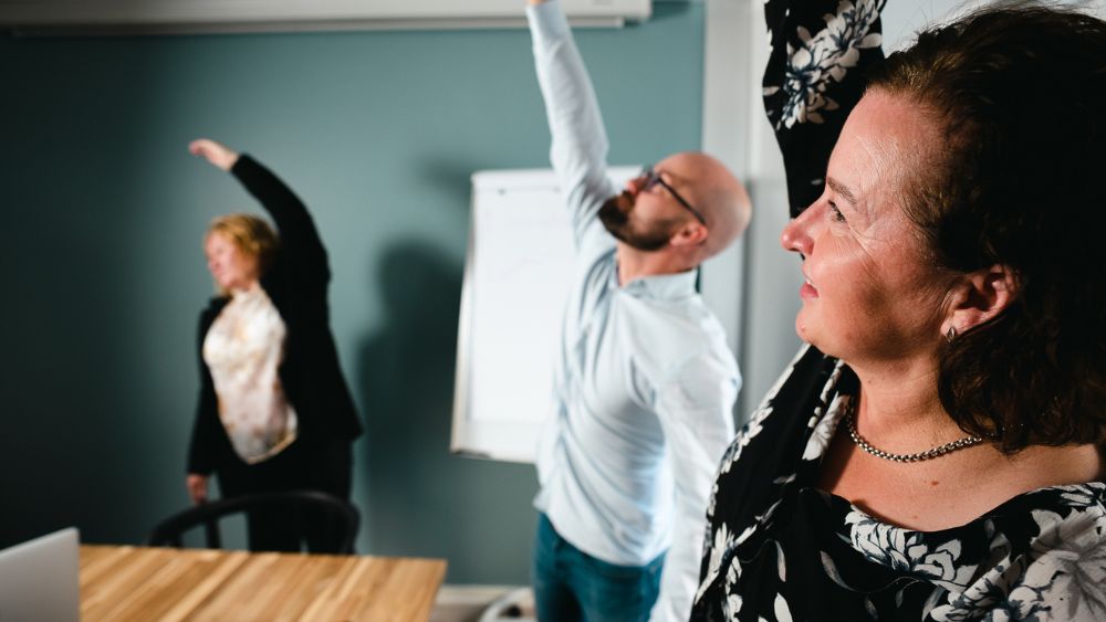 Kokouksen osallistujat pitävät taukoa ja venyttelevät kylkiä seisten.