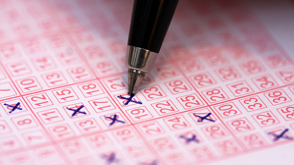 Kynää pitelevä käsi. Täytetty paperinen lottokuponki.