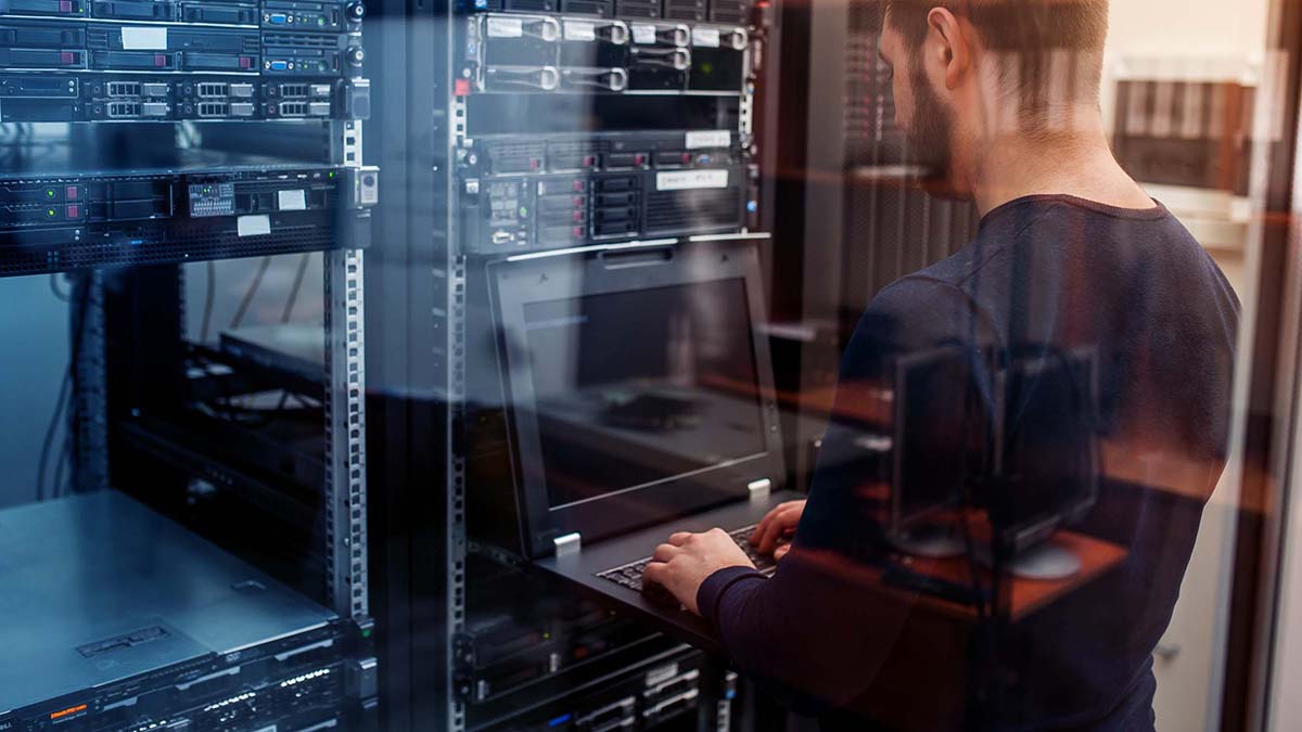 IT specialists work with a laptop in the server room, in the center of server racks and network devices.