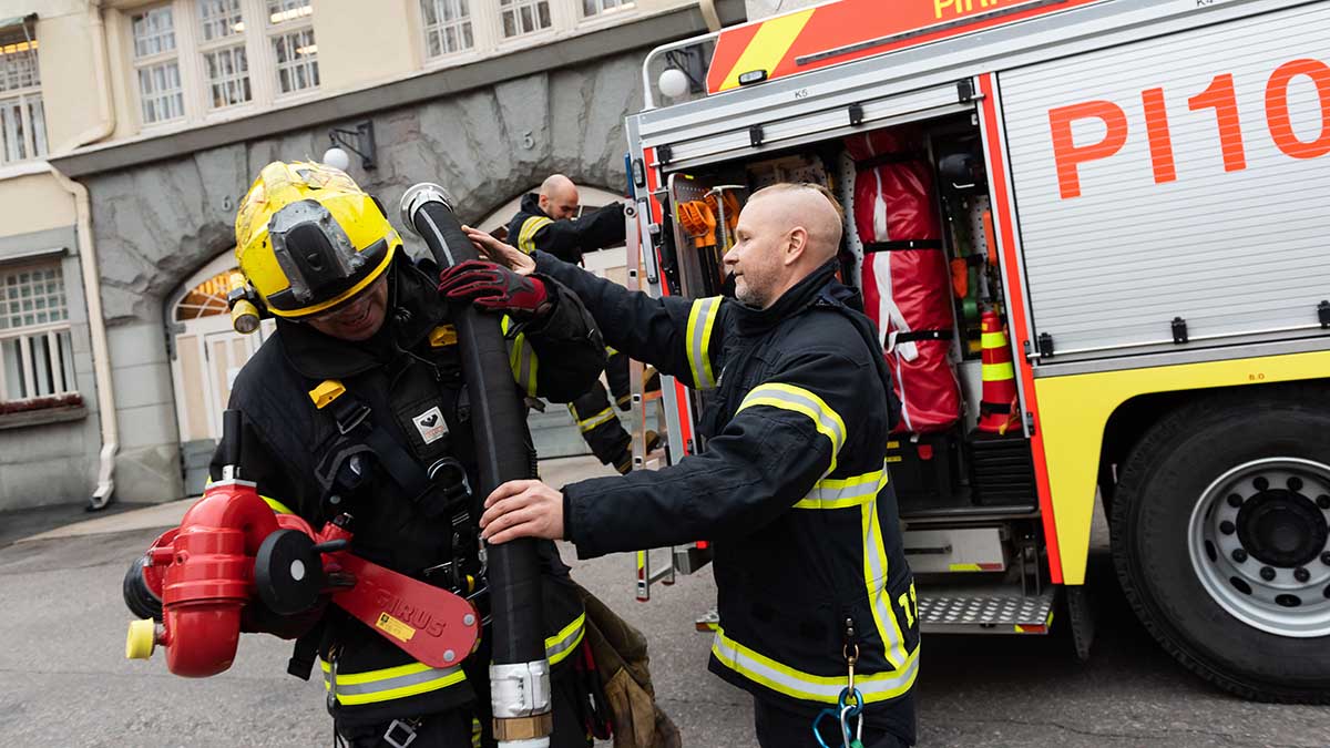 Pelastajat paloauton luona. Yhdellä pelastajista sammutusletku olkapäällä.