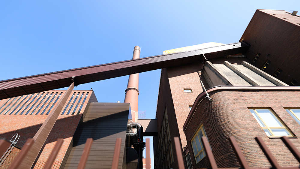 Kuvassa on punatiilinen energiantuotantolaitos korkeine savupiippuineen.