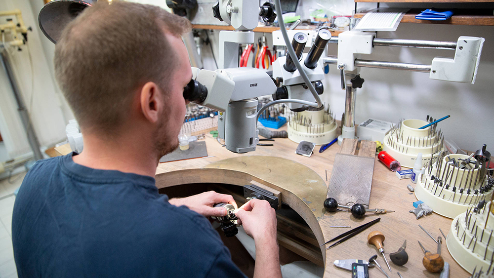 Kultaseppä tarkastelee käsissään pitelemää korua laitteellaan.