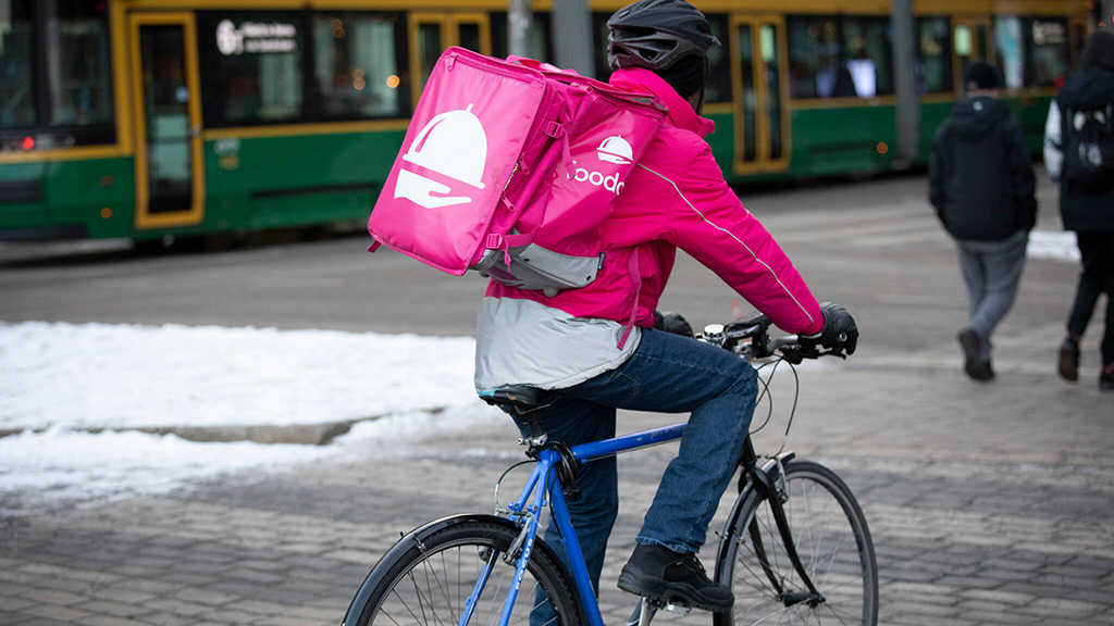 Kuvassa pyöräilee ruokalähetti viemässä annosta asiakkaalle.