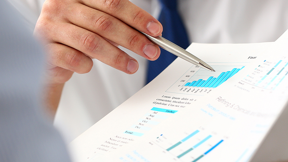 Kuvassa näkyy kynää pitelevä käsi ja paperilla olevia laskelmia.