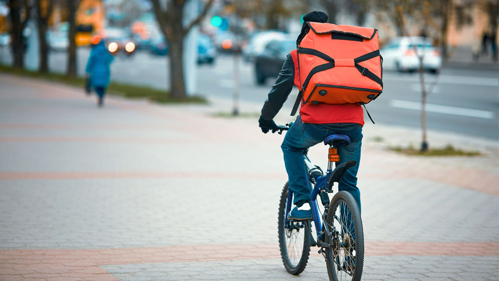 Kuvassa on ruokaa tai tavaraa pyörällä kuljettava lähetti