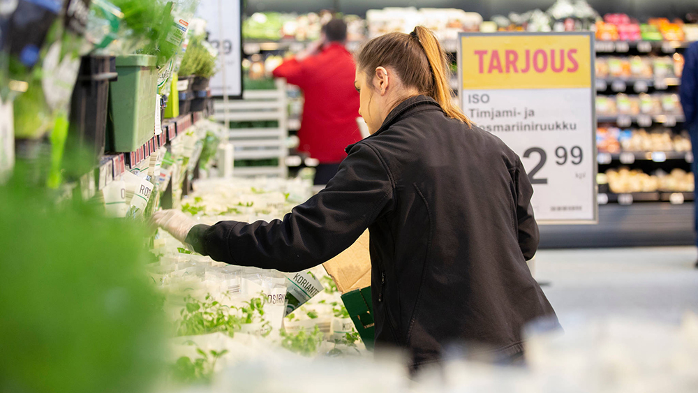 Myyjä laittamassa kasviksia hyllyyn kaupassa