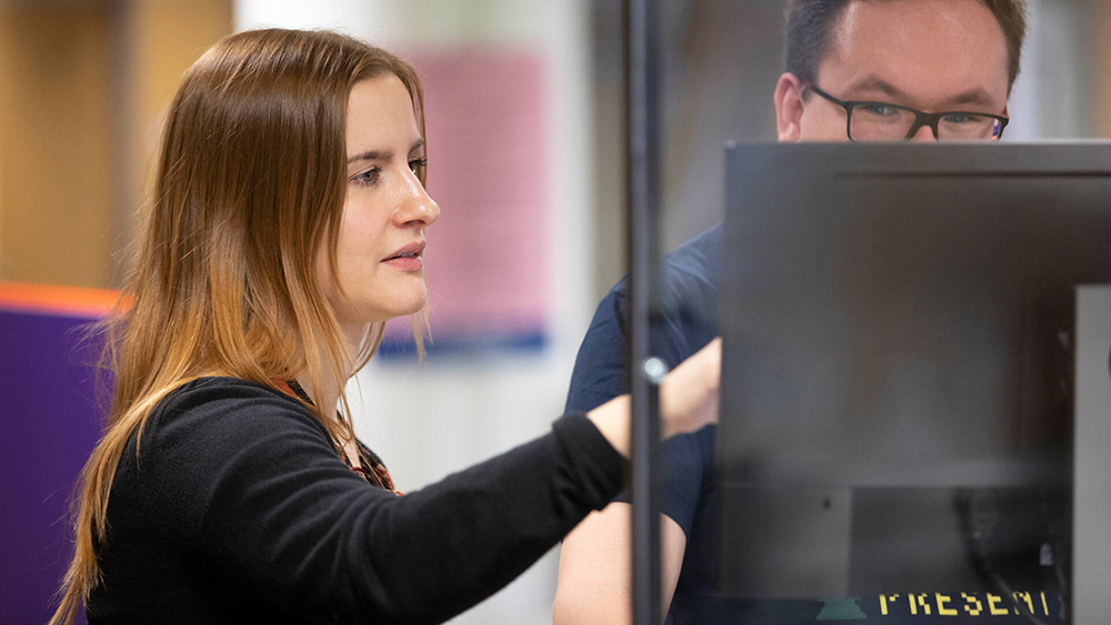 Kuvassa henkilö auttaa toista henkilöä tietokoneen sisällön käytössä.