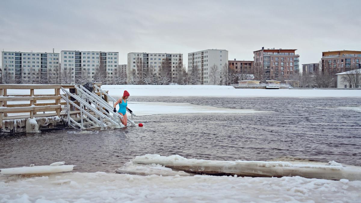 Kuvassa avantouimari laskeutuu veteen. Taustalla kaupunkinäkymä kerrostailoineen.