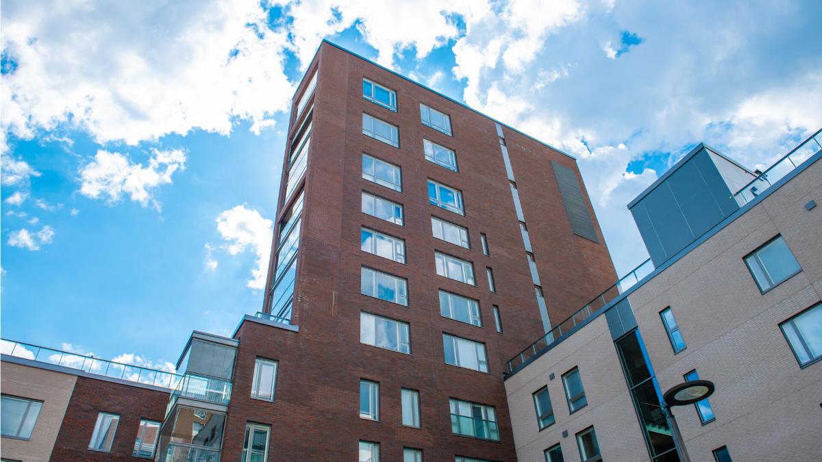 Punatiilinen ja vaalea kerrostalorakennus kirkasta taivasta vasten. Rakennuksessa on isoja ikkunoita ja parvekkeita. Näkymä alaviistosta ylöspäin.