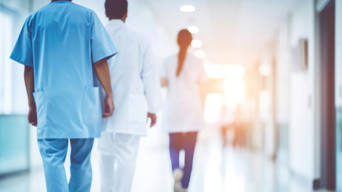 Hospital staff walking down the hallway away from the camera.