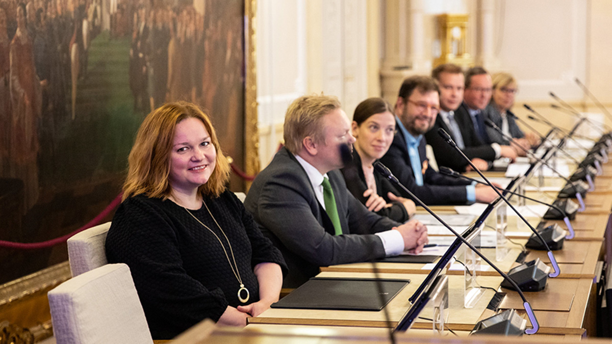 Kuvassa ministeri Krista Kiuru istuu valtioneuvoston istuntosalissa. Hänen vieressään istuu rivissä muita ministereitä.