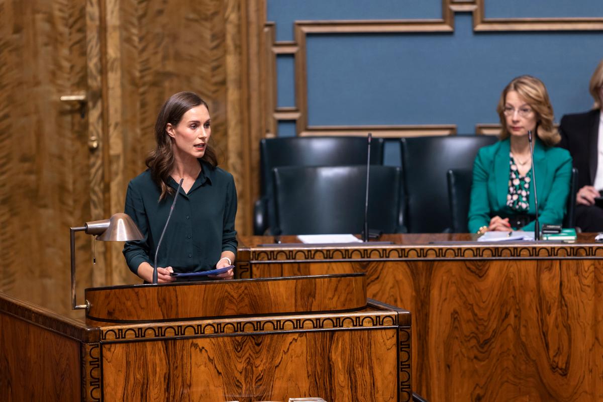 Pääministeri Sanna Marin puhumassa eduskunnan puhujanaitiossa. Ministeri Tuppurainen istuu vieressä hallituksen aitiossa.