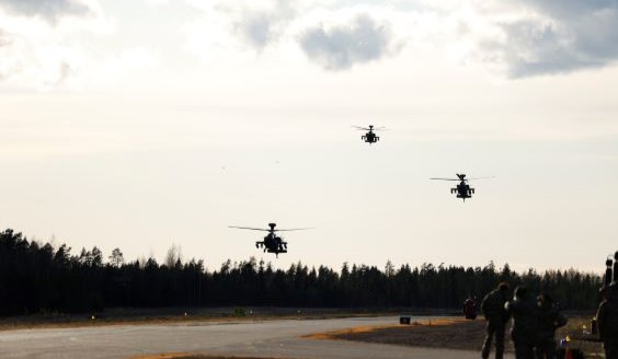Three helicopters in the sky coming to land.