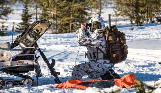 Talvisessa kuvassa lumipukuinen sotilas kiikaroi jonnekin kuvan ulkopuolelle. Sotilas on hyvin varusteltu, ja hänen rynnäkkökiväärinsä nojaa vieressään olevaa moottorikelkaa vasten.