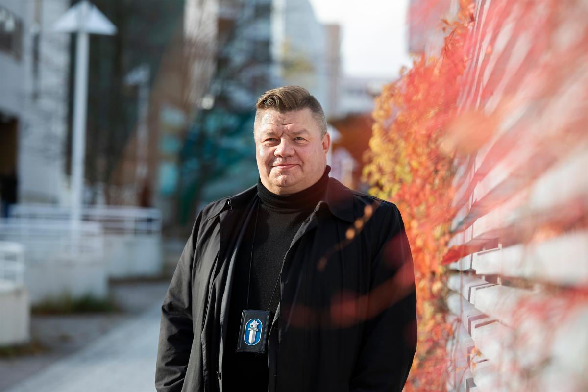 A police officer looks at a camera in an autumnal urban landscape.