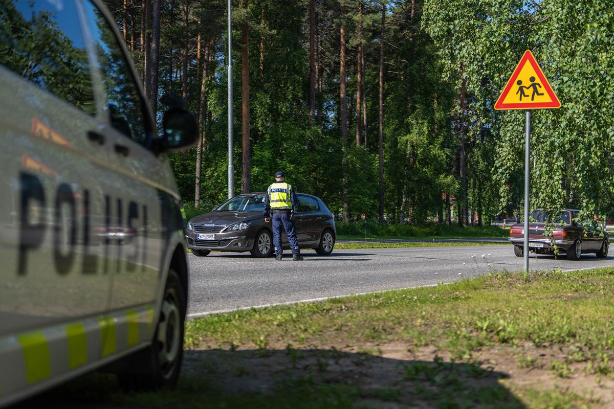 Poliisi pysäyttää autoa. Etualalla liikennemerkki, jossa varoitetaan lapsista liikenteessä.
