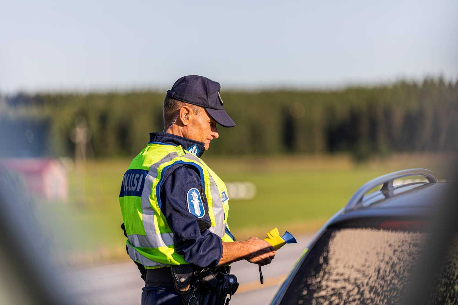 A police officer holding a breathalyser stands next to a car.