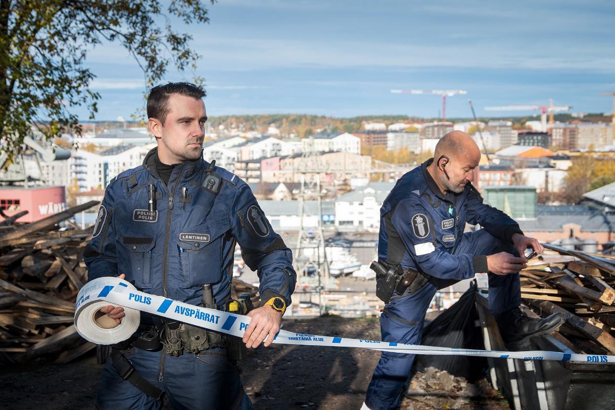 Lavastettu kuva kahdesta konstaapselista eristämässä rikospaikkaa.