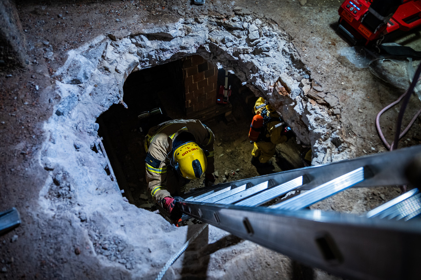 A firefighter descends a ladder into a pit.