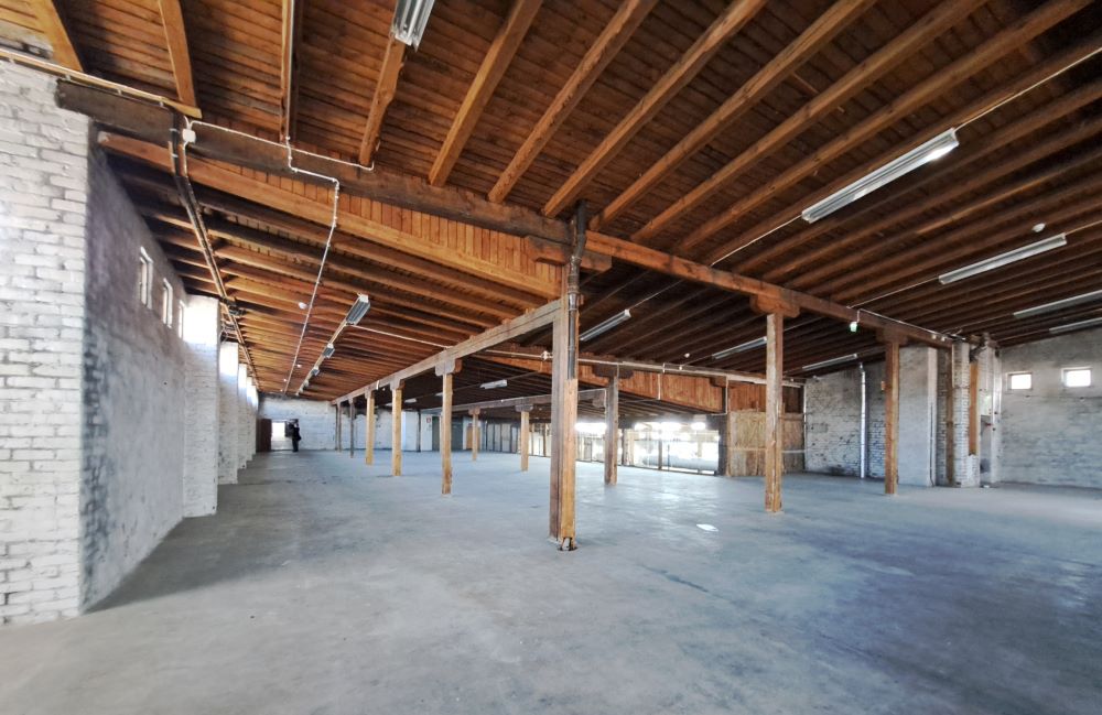 Illustrationen visar ett stort öppet utrymme i en gammal byggnad. Utrymmet har vita tegelväggar och trätak.