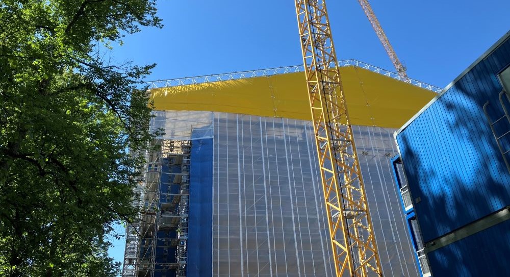 Illustrationen visar en byggnad skyddad med väderskyddstält på en byggplats.